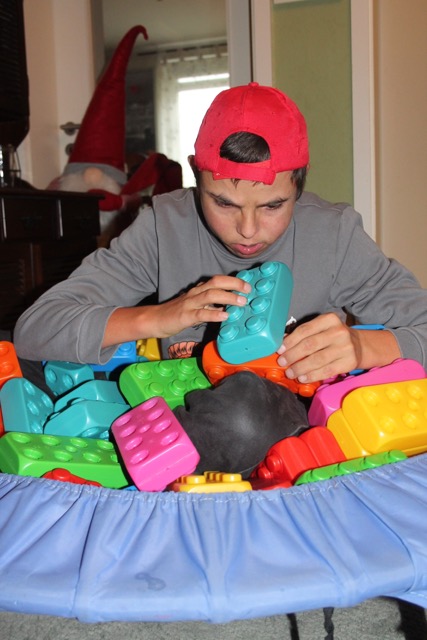 Ein junger Mann mit roter Kappe steckt konzentriert einen türkisfarbenen Playblock auf einen orangefarbenen Baustein.