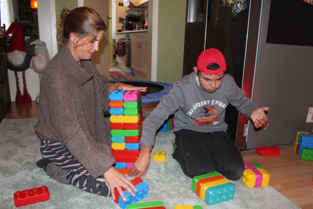 Eine Frau und ein junger Mann spielen gemeinsam mit Playblocks. Neben ihnen steht ein hoher bunter Turm.