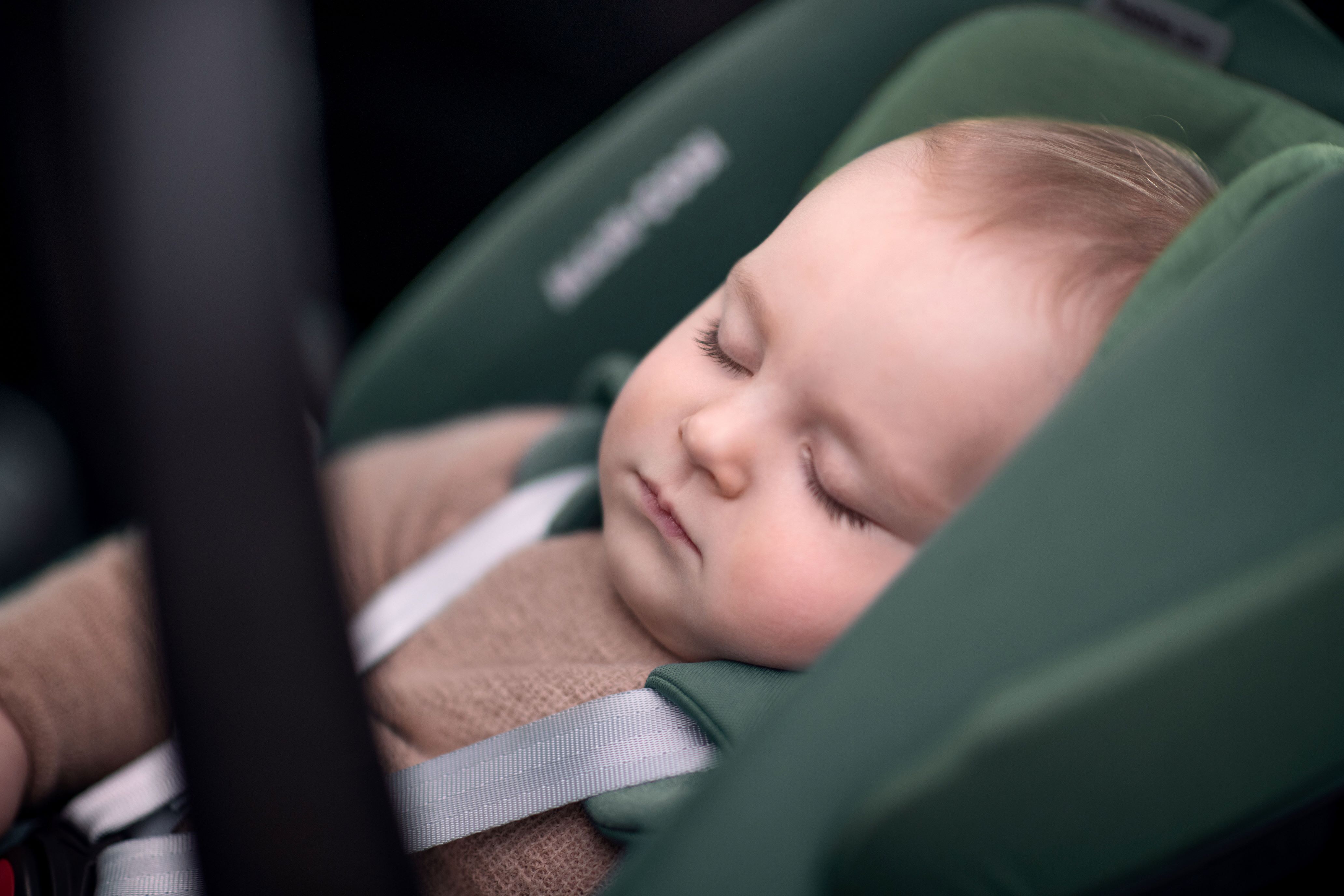 image Ein Baby schläft friedlich in einem grünen Maxi-Cosi Kindersitz, sicher angeschnallt und eingebettet in weiche Polster.