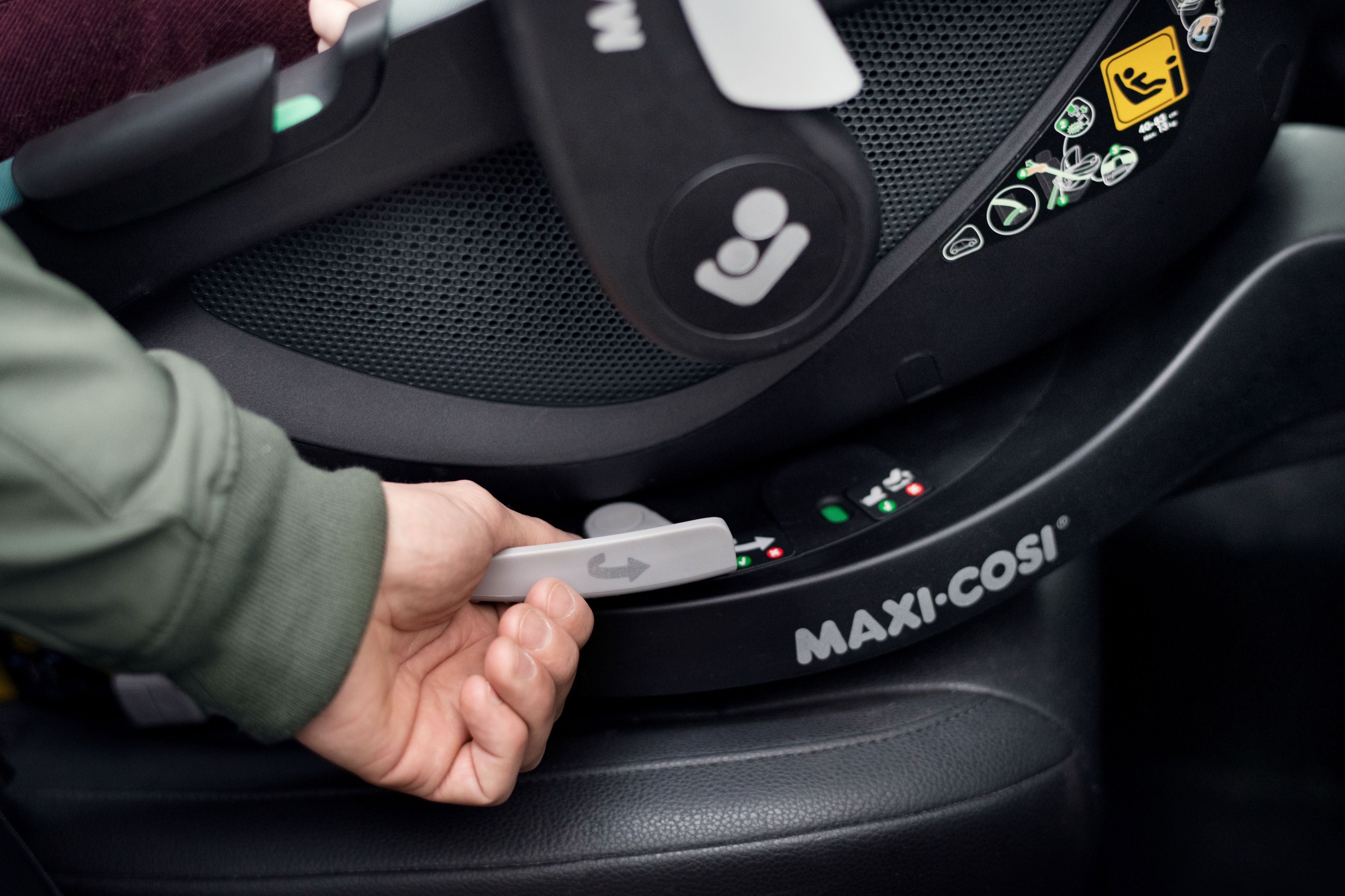 image Hand betätigt den Entriegelungsmechanismus an der Maxi-Cosi Basisstation, auf der eine Babyschale befestigt ist; die Indikatoren zeigen den korrekten Einbau an.